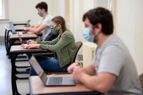 学生们在课堂上坐在笔记本电脑前，与社交保持距离. 学生们戴着口罩.